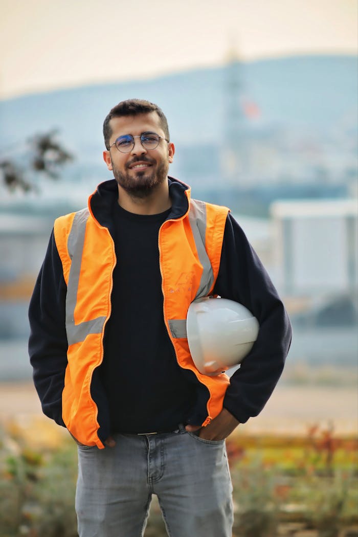 Confident male construction worker with safety vest and hard hat in a blurred outdoor setting.